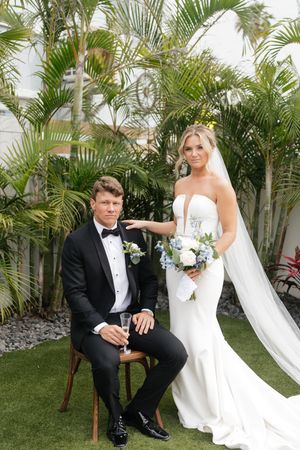 Elegant wedding portrait outdoors with tropical palm trees and lush greenery backdrop at a garden venue.