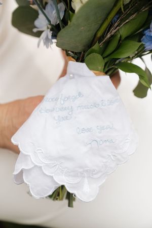 A white embroidered handkerchief with delicate lace trim tied to a green floral bouquet.