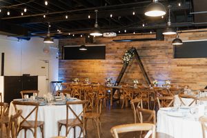 Modern rustic reception venue with wooden walls, crossback chairs, string lights and white tablecloths.