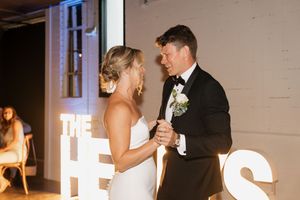A bride and groom share their first dance together at their wedding reception in front of illuminated letter decor.