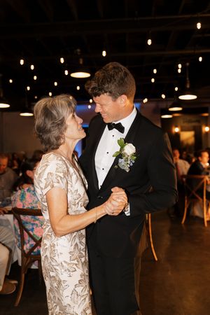 A couple dances together at a wedding reception under string lights in a rustic venue, sharing a romantic dance moment.