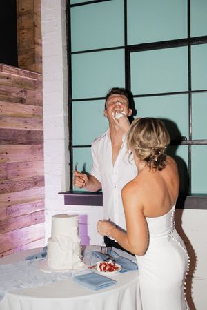 Newlywed couple shares a playful moment while cutting their wedding cake at a modern reception venue.