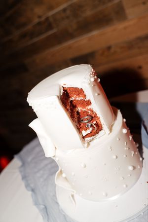 A white tiered wedding cake with pearl details reveals a red velvet interior through a cut slice.
