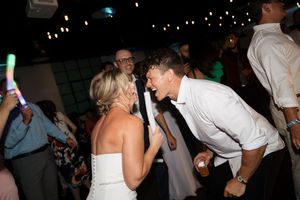 A couple in wedding attire share an energetic moment on a dimly lit dance floor during a celebration.