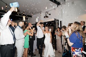 Celebration at a wedding reception with guests dancing under falling bubbles and bright lights in a dark venue.