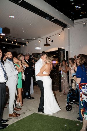A couple shares their first dance as newlyweds while wedding guests look on in an indoor venue with string lights.