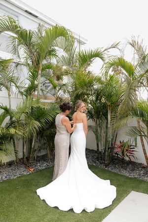 Two people in formal attire stand together against a tropical palm garden backdrop at an outdoor venue.