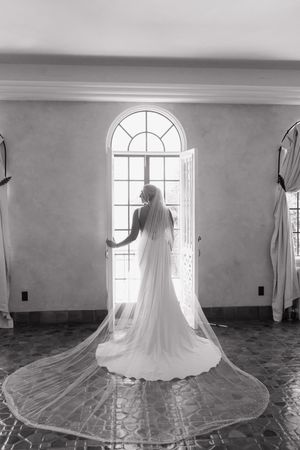 A sequence of black and white photos showing a wedding dress with a flowing cathedral veil in front of arched windows.