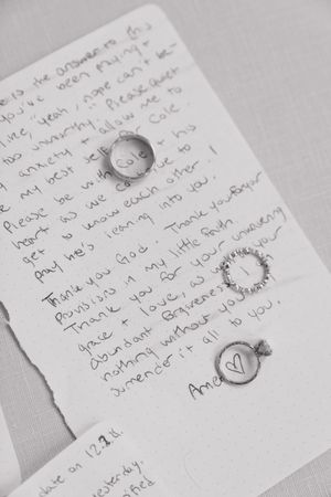 Handwritten note on white paper with two silver rings placed on top in black and white.