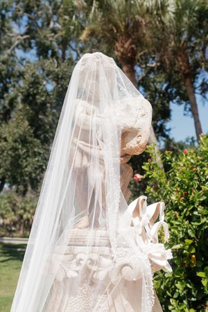 A delicate white bridal veil blows gracefully in the wind against a sunny garden backdrop with green foliage.