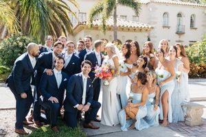 Wedding party poses outdoors at Mediterranean-style venue with palm trees and white stucco architecture.