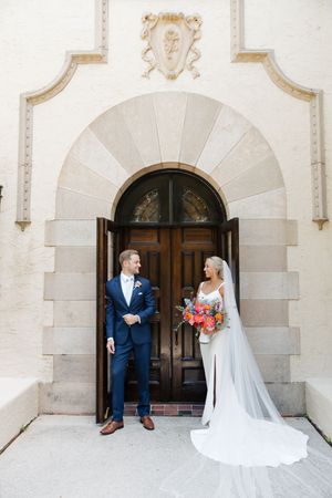 A classic wedding portrait in front of an elegant arched doorway with ornate architectural details.