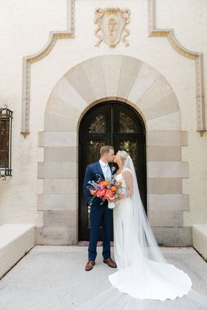 A romantic wedding moment captured beneath a stone archway with decorative details.
