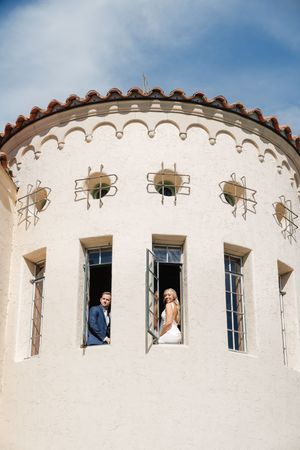 Wedding party members look out through windows of a circular white tower against blue sky.