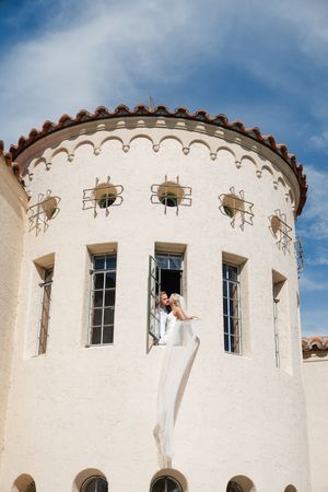 A person in a white dress poses in a window of a Mediterranean-style tower with ornate architectural details.