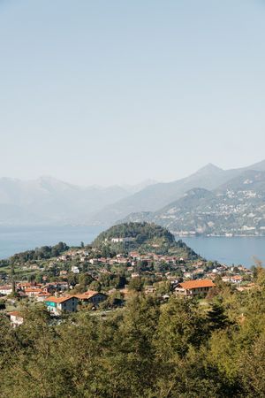 Aerial view of a picturesque Italian lakeside village with terracotta rooftops, lush greenery, and misty mountains by Lake Como.