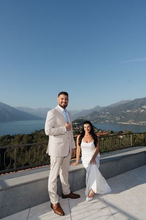 Bride and groom pose on a terrace overlooking a scenic lake and mountains on their wedding day.