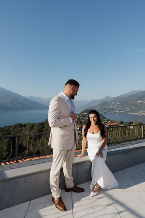Bride and groom sharing a romantic moment on a terrace with stunning mountain lake views behind them.