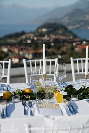 Elegant outdoor wedding table setting with candles, lemons, and a scenic lake view.