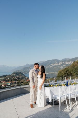 Wedding couple shares a kiss on terrace overlooking scenic Lake Como mountains.