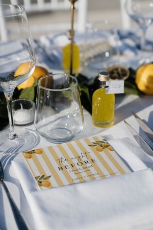 Elegant wedding rehearsal dinner table setting with lemon decor, glassware, and a yellow striped menu card.