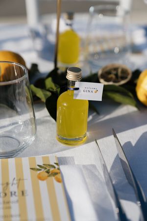 Small bottle of limoncello with a personalized name tag reading Gina on a elegantly set wedding reception table.
