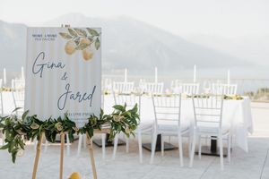 Elegant outdoor wedding ceremony setup with white chairs and a floral welcome sign for Gina and Jared by a scenic lake.