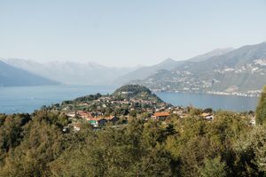 Aerial view of a picturesque lakeside village nestled among lush trees with mountains and blue water in the background.