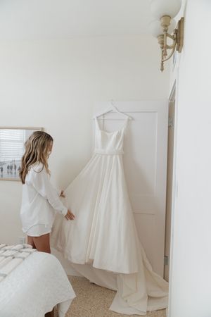 Multiple views showing an elegant white strapless wedding dress displayed on a wall against a light colored background.