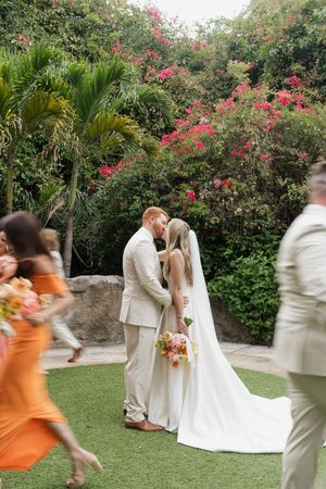 A couple share a romantic moment in a tropical garden with pink bougainvillea flowers and palm trees.