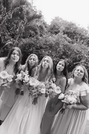 Five bridesmaids in light flowing dresses pose together holding white floral bouquets in a black and white photo.