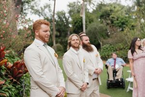 Wedding party members in cream-colored suits stand together during an outdoor garden ceremony.