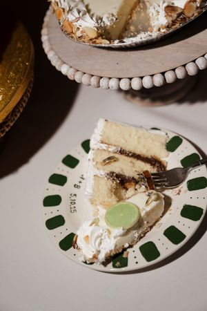 A slice of layered white cake with cream filling sits on a decorative plate with green accents and a silver fork.