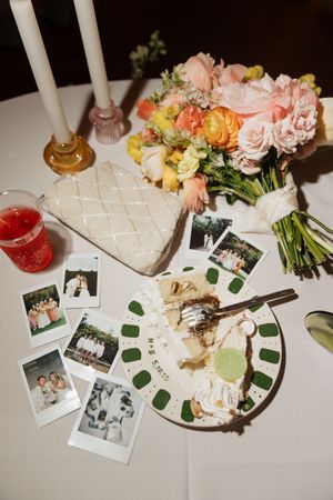 Wedding reception table setting with floral arrangements, Polaroid photos, and decorative candles in soft lighting.