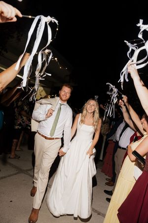 Wedding couple makes their grand exit as guests wave white ribbon streamers during nighttime celebration.