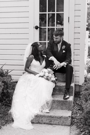 A joyful newlywed couple sits together on church steps in a candid black and white wedding photograph.