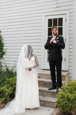 Bride in flowing white veil and groom in black suit pose separately on church steps during wedding photo session.