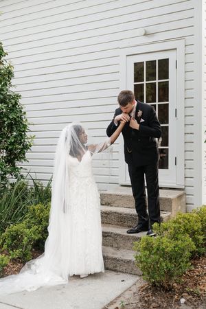 A romantic wedding moment captured on white church steps with a bride in lace gown and groom in black suit.