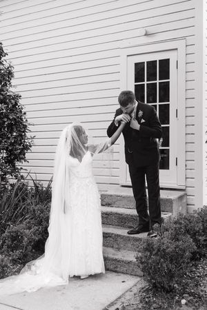 Couple in wedding attire have an emotional first-look moment outside a white church building.