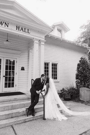 A wedding couple shares a romantic moment on the steps of a white historic Town Hall building.