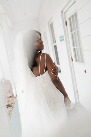 A romantic bridal portrait in a flowing white lace gown standing in a bright sunlit hallway.