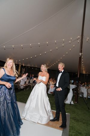 Bride and groom laughing with guest under elegant white tent with string lights at wedding reception.