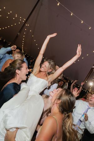 Bride in white gown dancing joyfully with bridesmaids at a festive wedding reception under fairy lights.