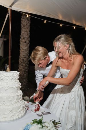 Bride and groom cutting their white tiered wedding cake together at an outdoor evening reception.