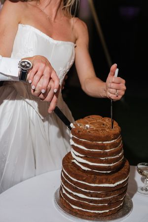 Bride and groom cutting a rustic naked layered chocolate wedding cake with white frosting.