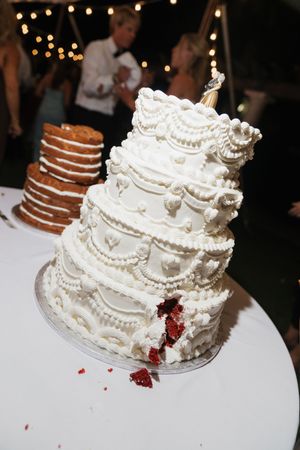 Elegant white four-tier wedding cake with intricate piped details and red velvet interior revealed after cutting.