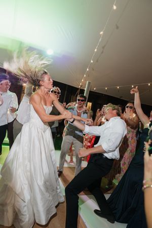 Bride and guest dancing wildly with hair flying at a fun wedding reception under a white tent.