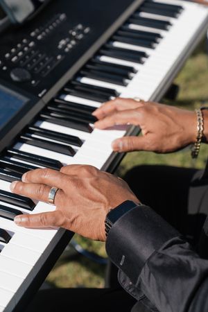 Close-up of musician's hands playing electronic keyboard piano at outdoor wedding event.