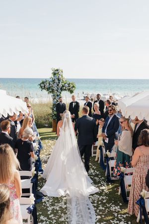 Aerial view of bride walking down aisle at beachfront wedding ceremony with ocean backdrop.
