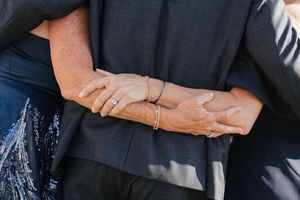 Close-up of couple embracing showing elegant bracelets and rings against navy blue wedding attire.
